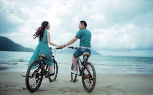 海辺で手を繋ぐ自転車に乗ったカップル